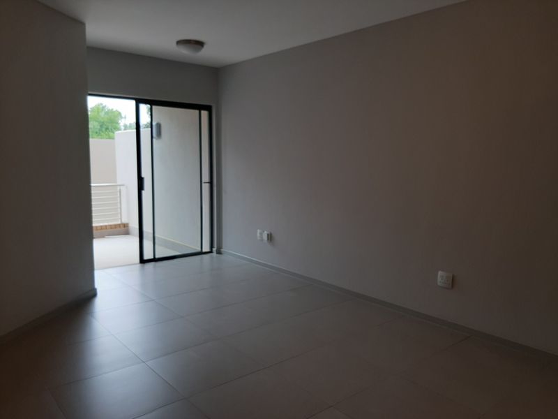 An empty, neutral-toned living area featuring large format floor tiles and a sliding glass door providing access to an outdoor balcony space.