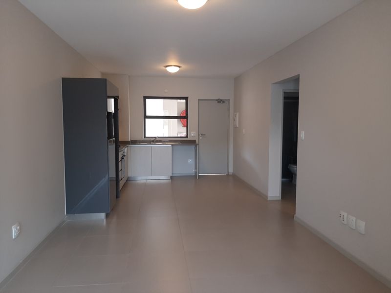 An open-plan living and kitchen area featuring neutral tiled flooring, modern cabinetry, and a functional layout in a well-maintained apartment.