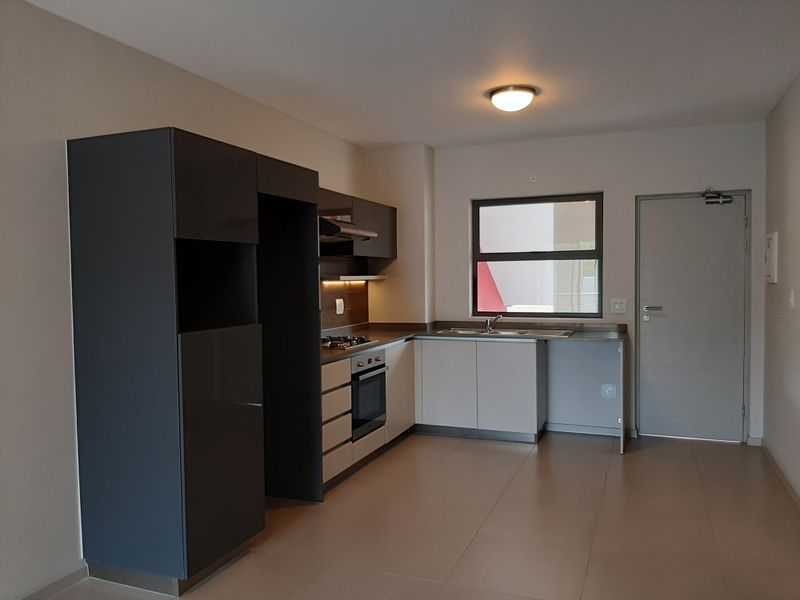 Modern kitchen featuring sleek two-tone cabinetry, built-in gas hob, electric oven, extractor fan, and stainless steel sink with tiled flooring.