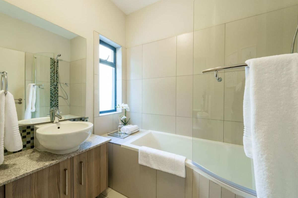 Modern bathroom featuring a vessel sink on a granite vanity, a bathtub with a glass shower screen, and neutral wall tiling.