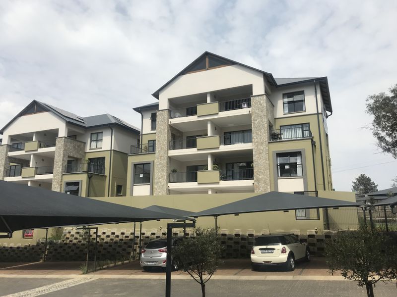 A multi-story apartment complex featuring stone-clad accents, private balconies, and dedicated covered parking bays within a well-maintained residential estate.