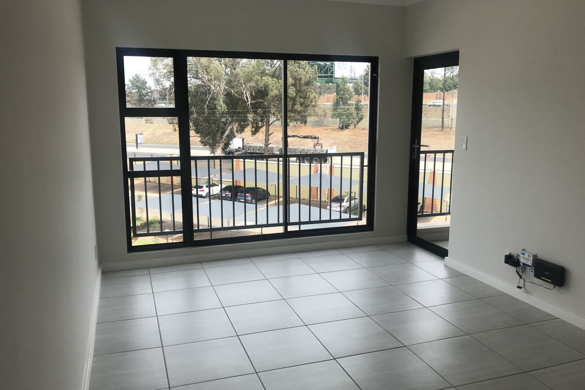 A bright, empty living area featuring modern tiled flooring and large aluminium sliding doors that open onto a balcony.