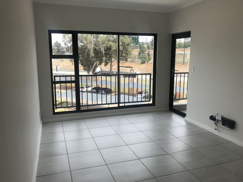 A bright, empty living area featuring modern tiled flooring and large aluminium sliding doors that open onto a balcony.