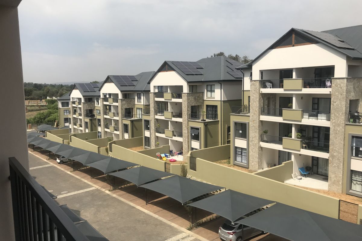 Elevated view of a modern apartment complex featuring multi-story units with balconies, stone accents, solar panels, and dedicated covered parking bays.