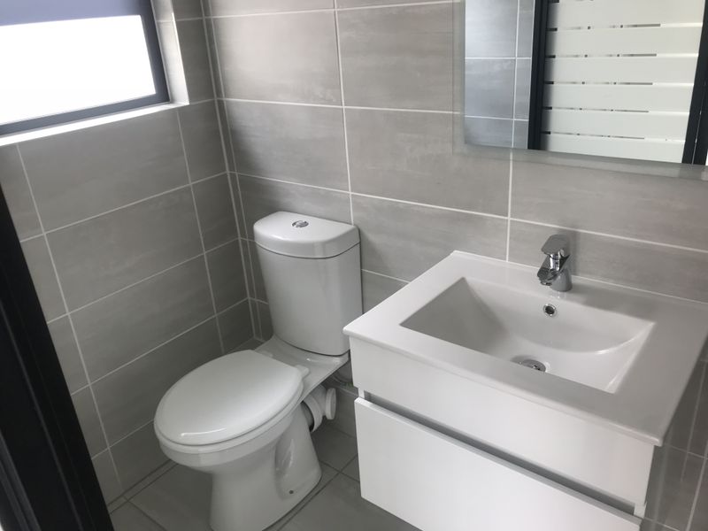 A modern, well-maintained bathroom featuring neutral wall and floor tiling, a contemporary vanity with basin, and a wall-mounted mirror.