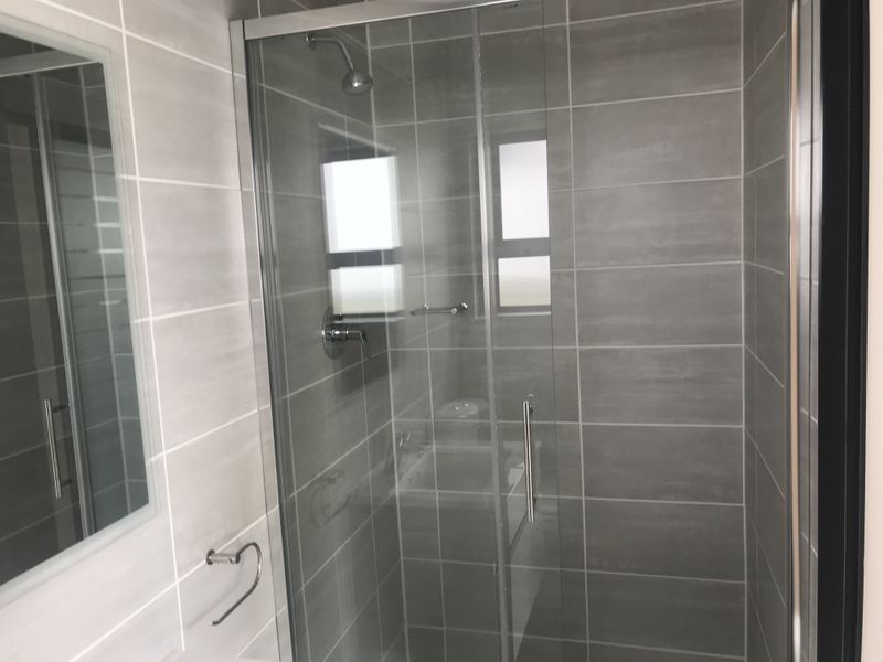 A modern bathroom featuring a glass-enclosed shower with grey wall tiling and chrome fixtures.