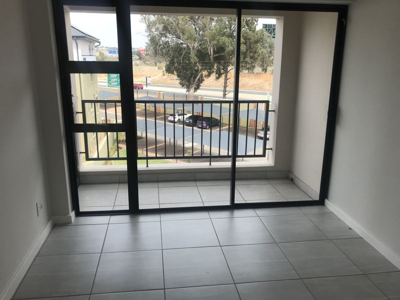 A clean, empty balcony featuring modern grey floor tiles and a secure metal balustrade, accessible through a large sliding glass door.