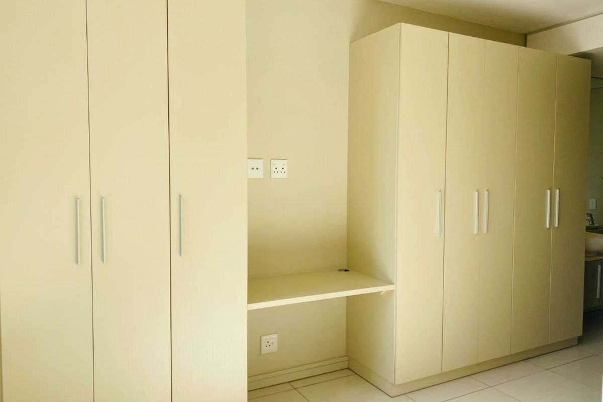 A clean bedroom interior featuring extensive built-in cabinetry and a integrated desk area with neutral finishes and tiled flooring.