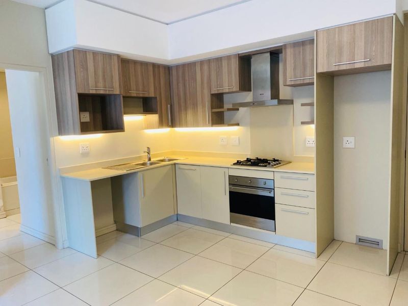 Modern kitchen featuring light-toned cabinetry, integrated stainless steel appliances, gas hob, extractor fan, and tiled flooring with under-cabinet lighting.