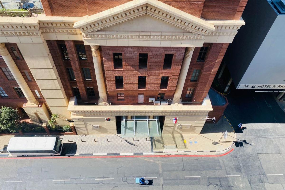 Aerial view of a classic brick apartment building facade featuring architectural columns, a pediment, and a modern glass entrance canopy.