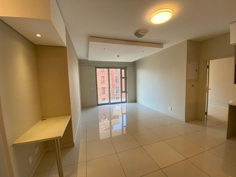 A bright, open-plan living area featuring polished tile flooring, a recessed ceiling with downlights, and a built-in desk, leading to a sliding glass door.