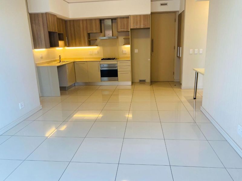Modern open-plan kitchen featuring sleek cabinetry, stone countertops, integrated appliances, and polished porcelain floor tiles in a bright, contemporary apartment setting.