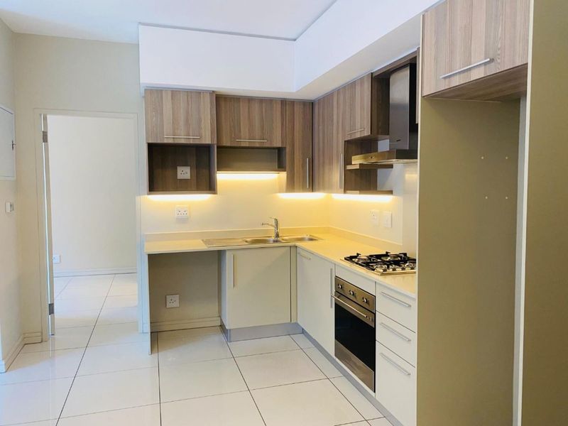Modern kitchen featuring built-in cabinetry, stainless steel oven and hob, extractor fan, and under-cabinet lighting with clean tiled flooring.
