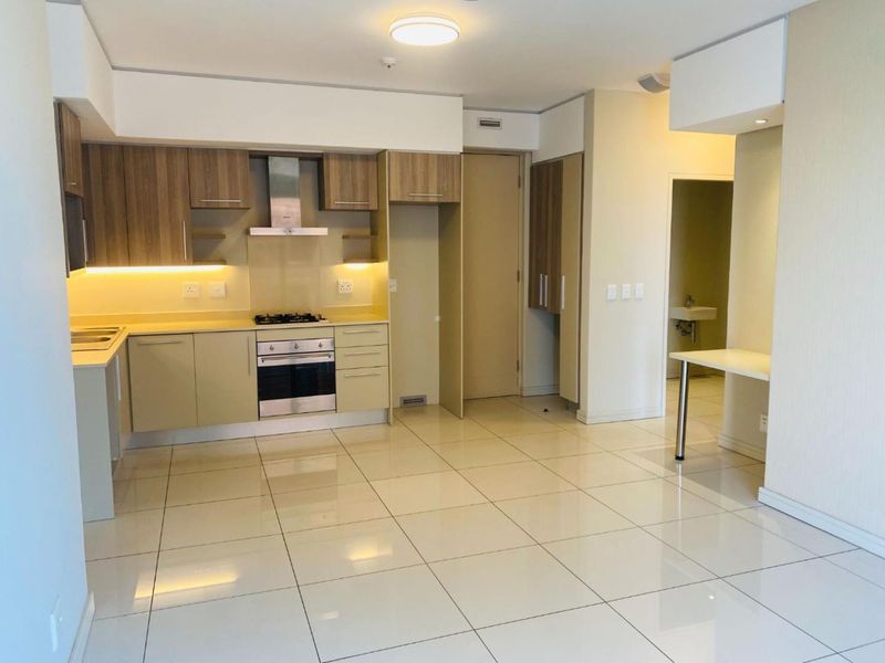 Modern open-plan kitchen featuring sleek cabinetry, stone countertops, and integrated appliances, seamlessly flowing into a spacious living area with polished tiled flooring.