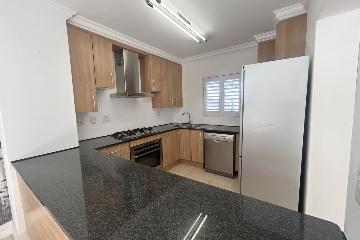 Functional kitchen featuring granite countertops, light wood cabinetry, built-in oven, gas hob, stainless steel extractor fan, and tiled flooring.