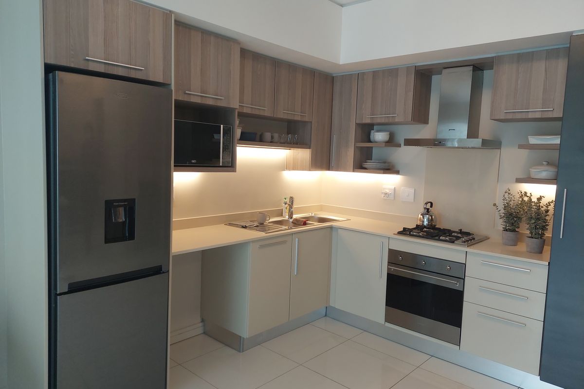 Modern kitchen featuring sleek cabinetry, stone countertops, integrated stainless steel appliances, gas hob, and under-cabinet lighting with polished tiled flooring.
