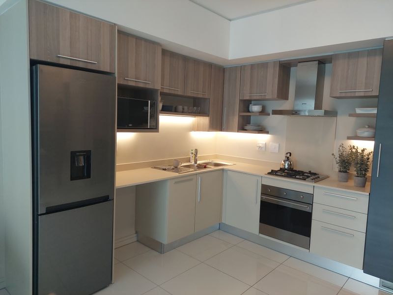 Modern kitchen featuring sleek cabinetry, stone countertops, integrated stainless steel appliances, gas hob, and under-cabinet lighting with polished tiled flooring.