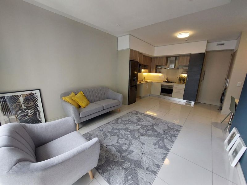 Modern open-plan living area featuring a compact, well-equipped kitchen with built-in cabinetry, integrated appliances, and sleek tiled flooring throughout.