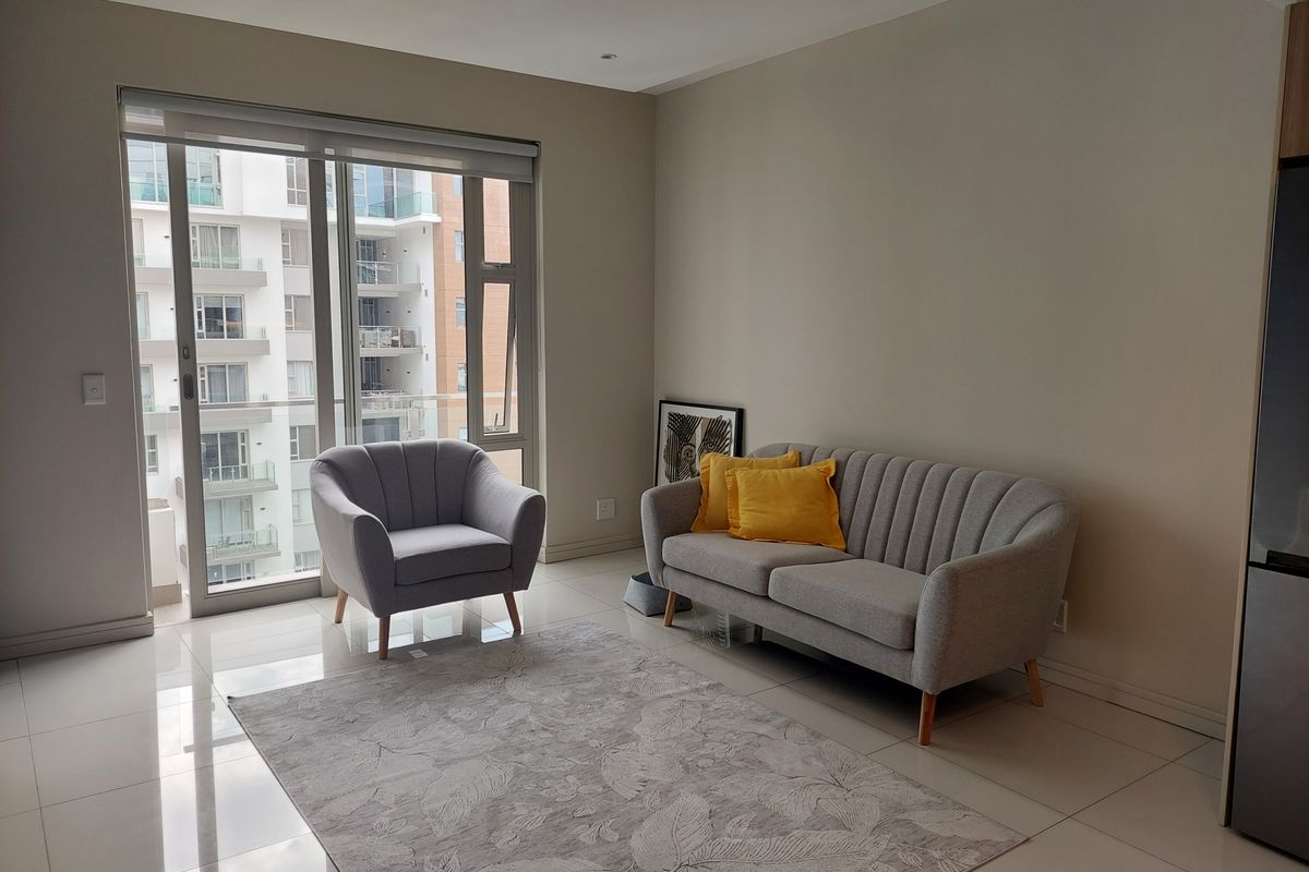 A bright living room featuring neutral tiled flooring, recessed lighting, and a large sliding glass door providing access to the balcony.