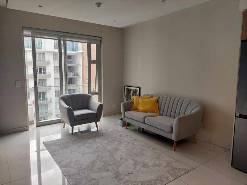 A bright living room featuring neutral tiled flooring, recessed lighting, and a large sliding glass door providing access to the balcony.