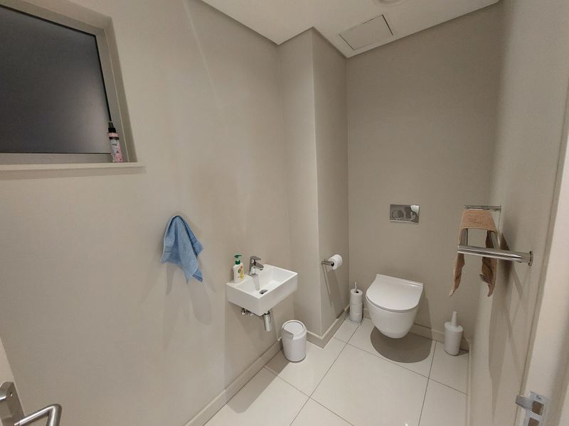 A modern guest bathroom featuring a wall-mounted toilet with a concealed cistern, a compact wall-mounted basin, and neutral tiled flooring.