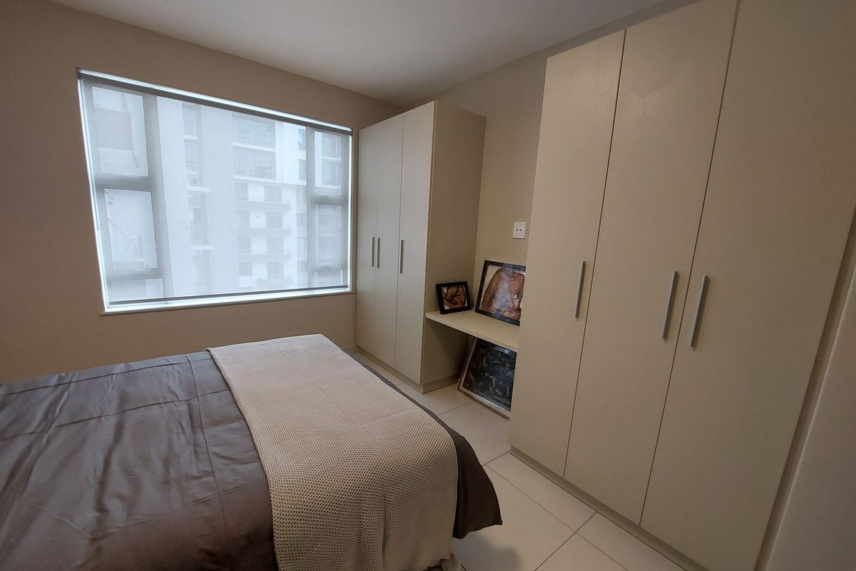 A well-maintained bedroom featuring neutral tiled flooring, ample built-in cupboard storage, and a large window providing natural light.