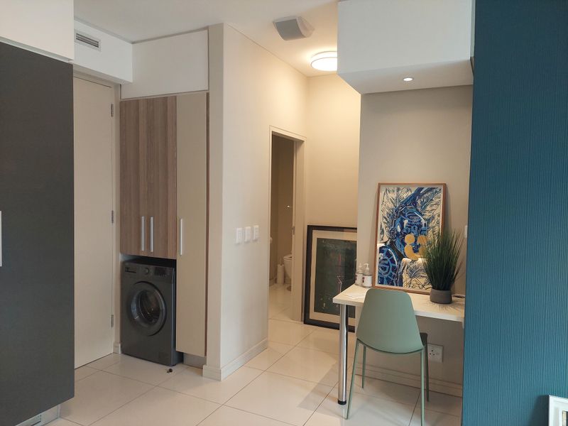 A well-maintained hallway featuring built-in cabinetry with an integrated laundry space, tiled flooring, and recessed lighting, leading towards a bathroom.