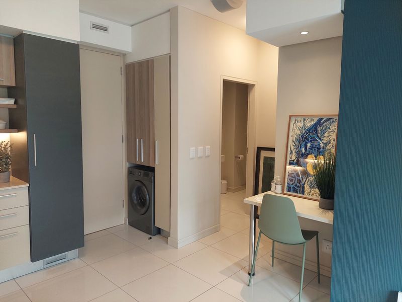 Modern open-plan apartment interior featuring tiled floors, built-in cabinetry with integrated laundry space, and recessed lighting leading to a bathroom.