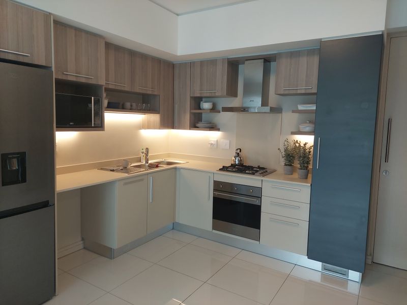 Modern kitchen featuring sleek cabinetry, integrated stainless steel appliances, gas hob, extractor fan, and under-cabinet lighting with polished tiled flooring.