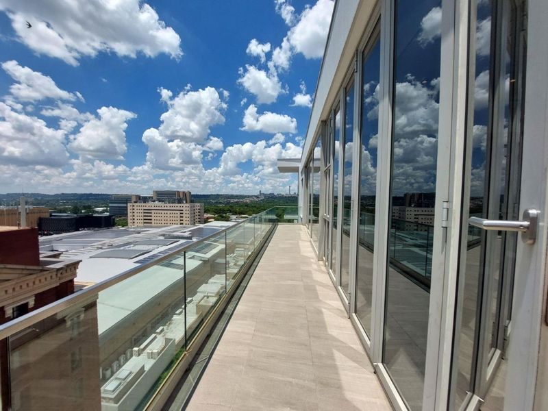 A spacious modern balcony featuring a sleek glass balustrade, tiled flooring, and expansive floor-to-ceiling glass doors offering panoramic city views.