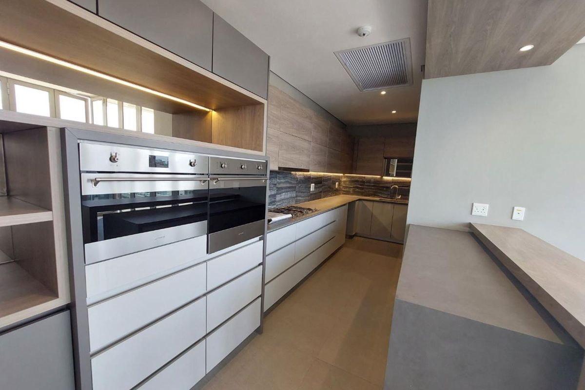 Modern kitchen featuring high-end cabinetry, built-in double ovens, gas hob, stone countertops, and integrated lighting in a sleek, contemporary design.