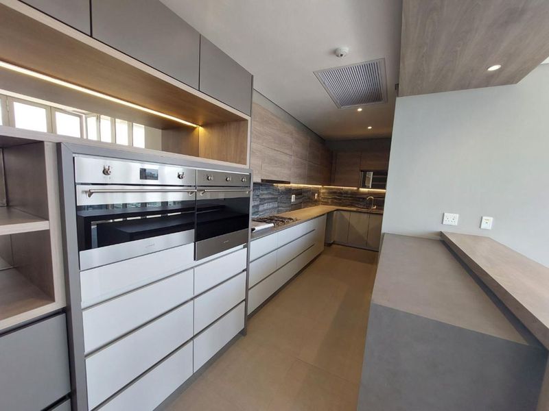 Modern kitchen featuring high-end cabinetry, built-in double ovens, gas hob, stone countertops, and integrated lighting in a sleek, contemporary design.