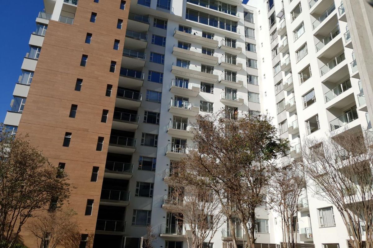A view of the rear facade of a modern multi-story apartment building featuring numerous balconies with glass balustrades and landscaped grounds.