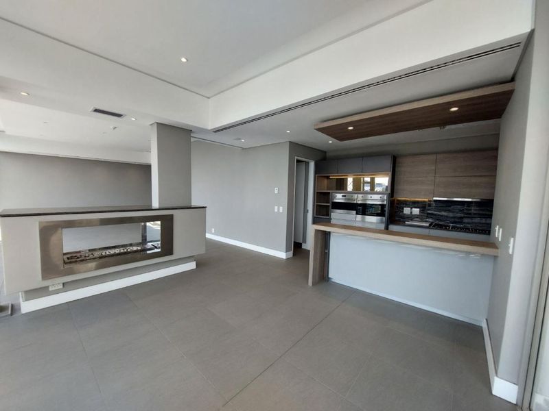 Modern open-plan living area featuring a sleek kitchen with built-in appliances, a breakfast bar, and a contemporary built-in fireplace.