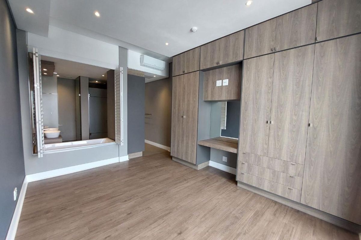 Spacious bedroom featuring extensive built-in cabinetry, integrated vanity, laminate flooring, and a large window opening into the en-suite bathroom.