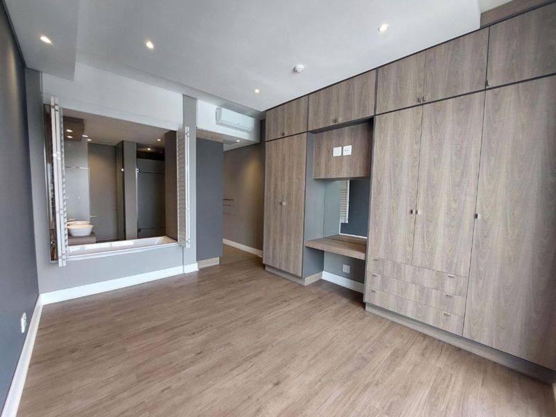 Spacious bedroom featuring extensive built-in cabinetry, integrated vanity, laminate flooring, and a large window opening into the en-suite bathroom.