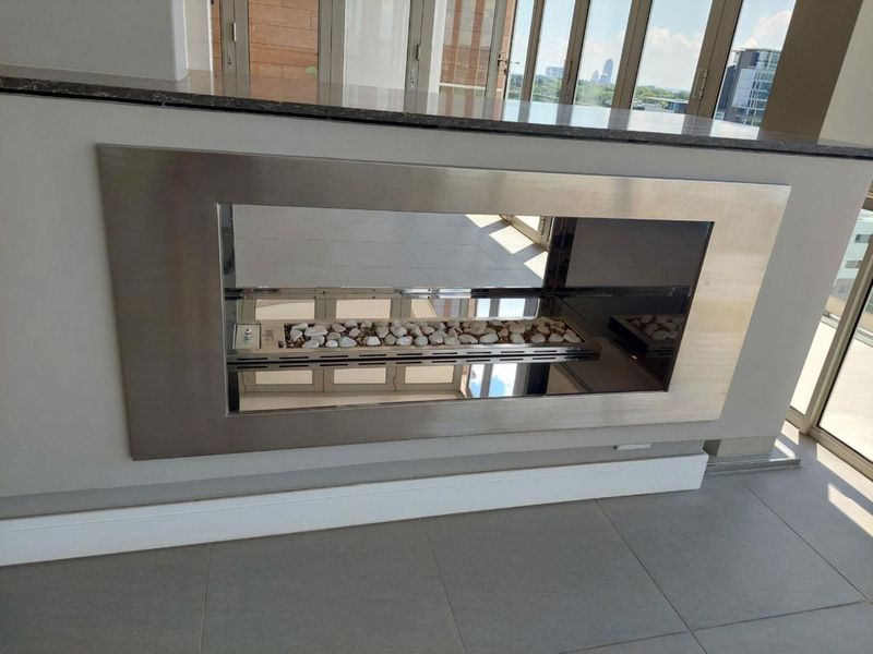 Modern living area featuring a sleek built-in fireplace with a stone countertop, tiled flooring, and large sliding glass doors leading to a balcony.