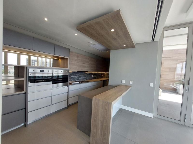 Modern kitchen featuring high-end integrated cabinetry, a built-in double oven, stone breakfast bar, and sleek recessed lighting with direct access to a balcony.