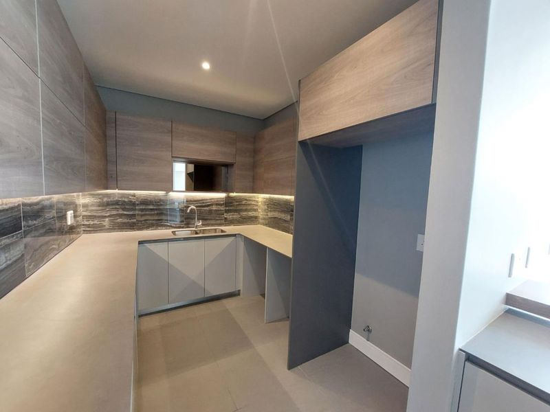 Modern kitchen featuring sleek wood-grain cabinetry, stone countertops, a tiled backsplash, and dedicated space for an integrated refrigerator.
