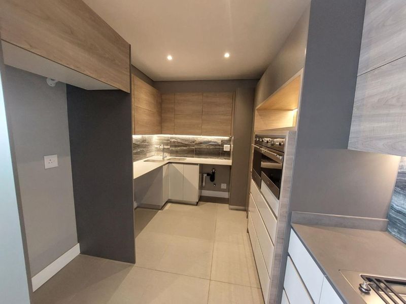 Modern, well-appointed kitchen featuring sleek wood-tone and grey cabinetry, integrated appliances, stone countertops, and contemporary under-cabinet lighting.