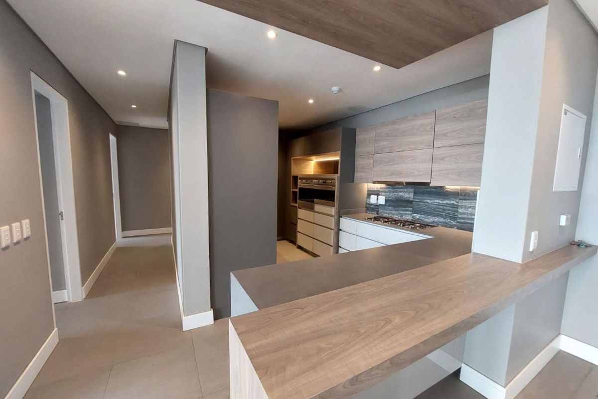 Modern kitchen featuring sleek wood-tone cabinetry, stone countertops, a breakfast bar, integrated oven, and gas hob, finished with contemporary recessed lighting and tiled floors.