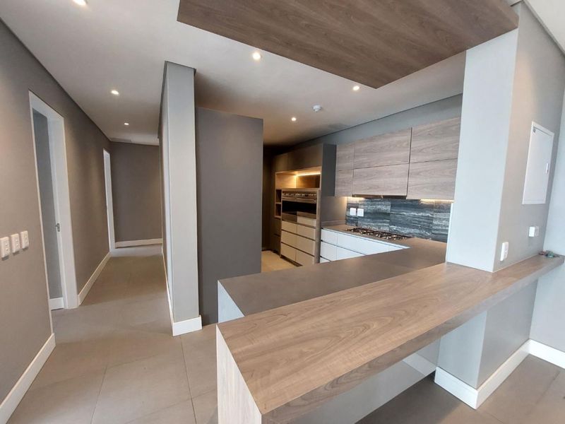 Modern kitchen featuring sleek wood-tone cabinetry, stone countertops, a breakfast bar, integrated oven, and gas hob, finished with contemporary recessed lighting and tiled floors.