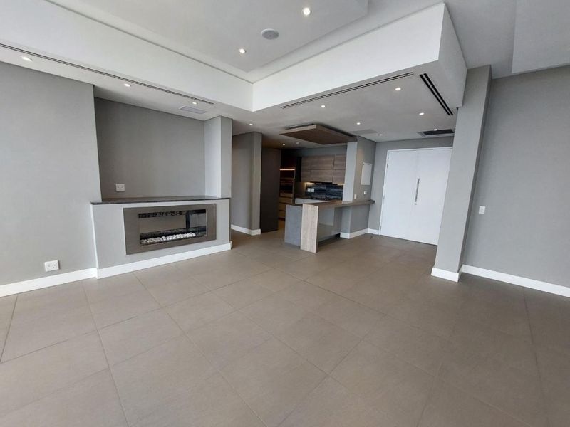 Spacious open-plan living area featuring a modern built-in fireplace, recessed ceiling lighting, and a sleek kitchen with integrated cabinetry and island.