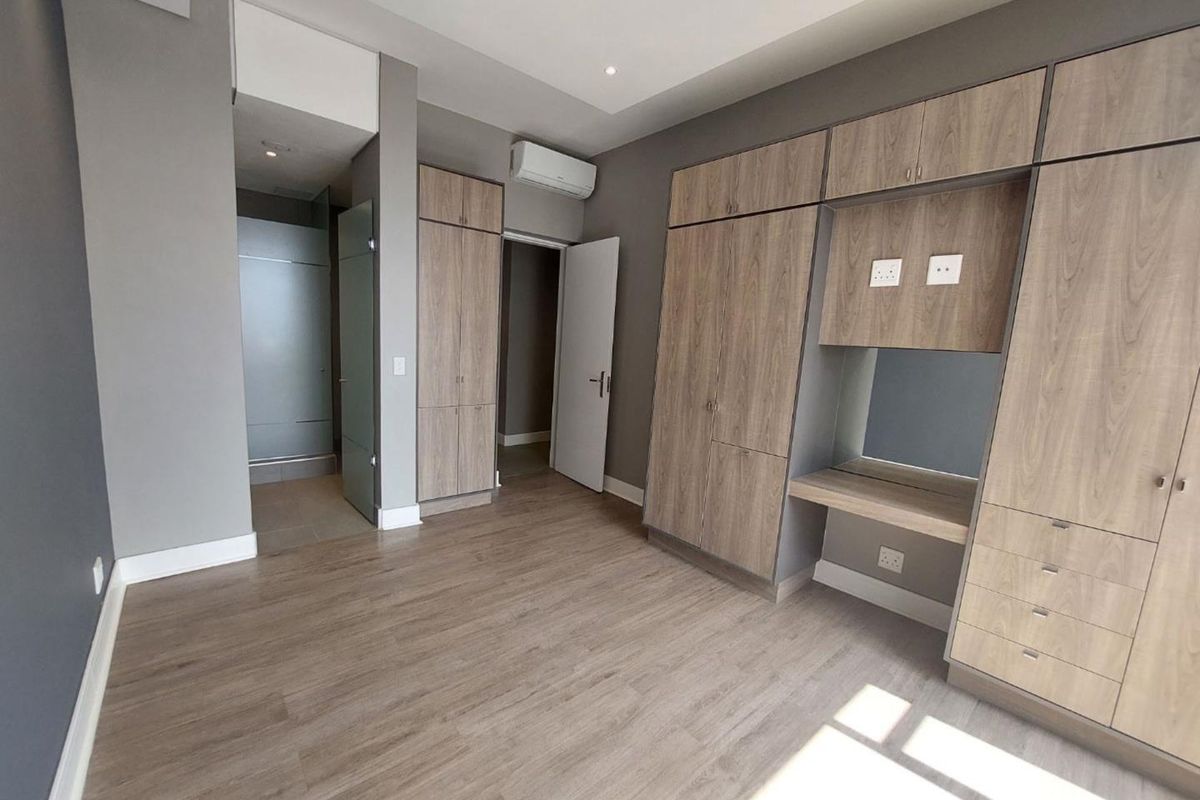 A modern, empty bedroom featuring extensive built-in cabinetry, a dedicated vanity area, laminate flooring, and a wall-mounted air conditioning unit.