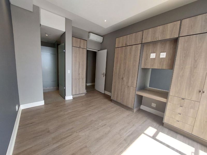 A modern, empty bedroom featuring extensive built-in cabinetry, a dedicated vanity area, laminate flooring, and a wall-mounted air conditioning unit.