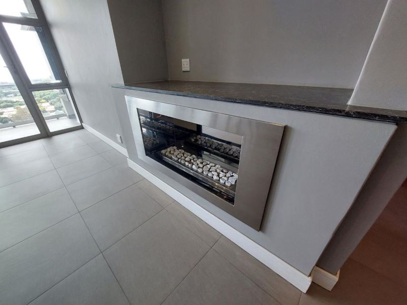 A modern living area featuring a sleek built-in fireplace with a stone mantel, neutral tiled flooring, and access to a balcony through glass doors.