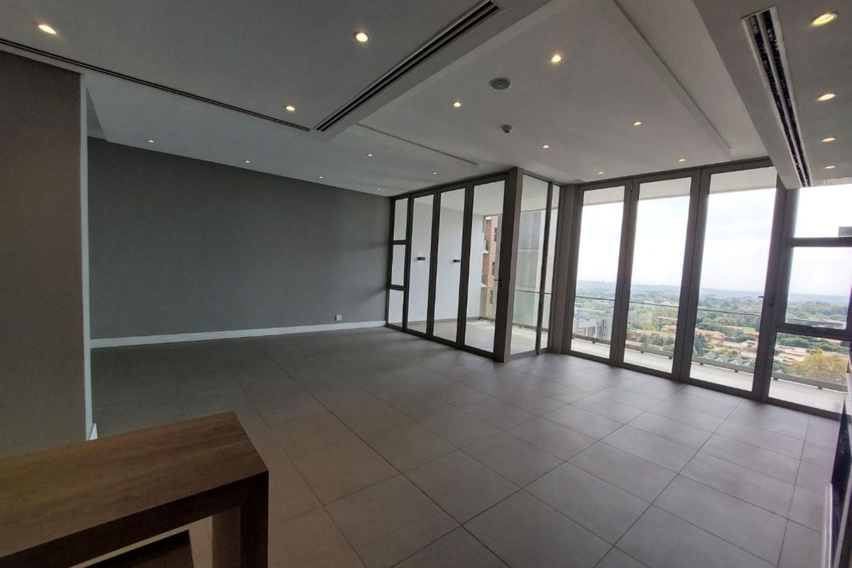 Spacious, modern open-plan living area featuring large glass sliding doors, recessed lighting, ducted air conditioning, and neutral tiled flooring with expansive views.
