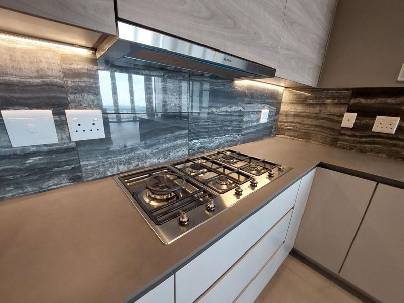 Modern kitchen featuring a high-end gas hob, stainless steel extractor fan, stone splashback, and sleek built-in cabinetry with integrated under-cabinet lighting.