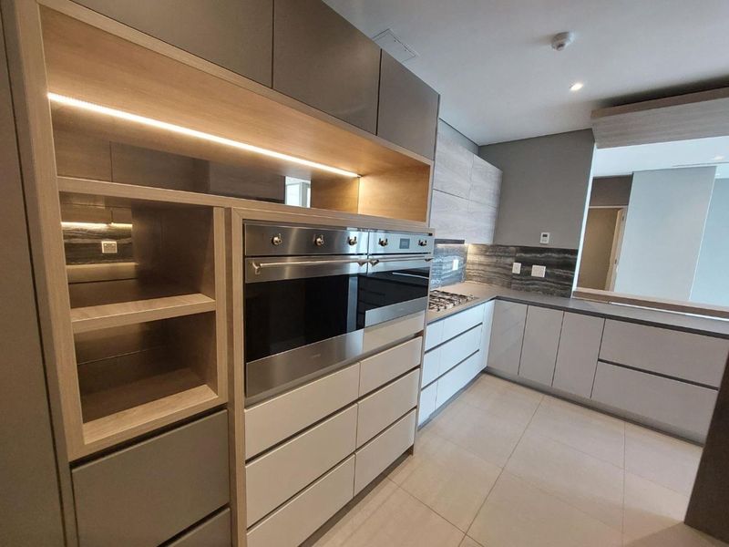 Modern kitchen featuring high-end integrated cabinetry, built-in oven, gas hob, stone countertops, and sleek under-cabinet lighting in a clean, contemporary finish.