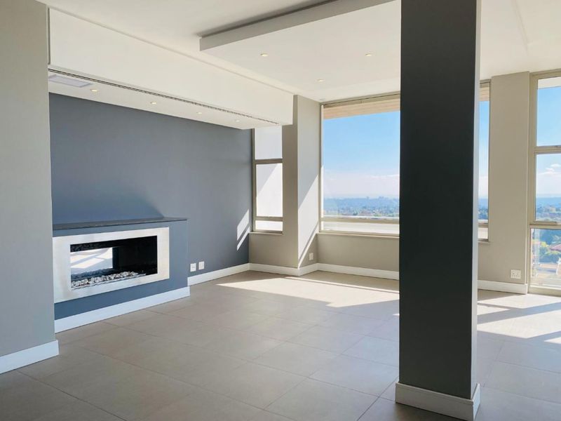 A bright, modern, and empty living room featuring a built-in fireplace, large windows with expansive views, and neutral tiled flooring.